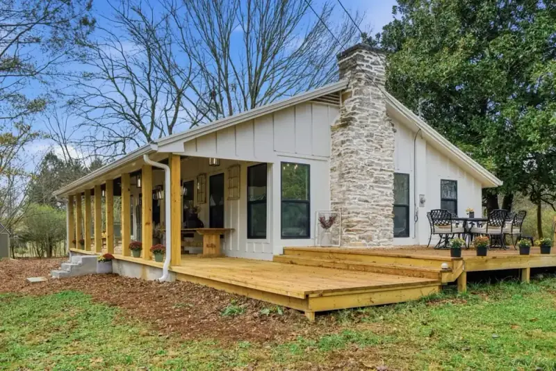 Curbside view of 356 Hyde Road with a wraparound covered porch, stone chimney, and wooded yard