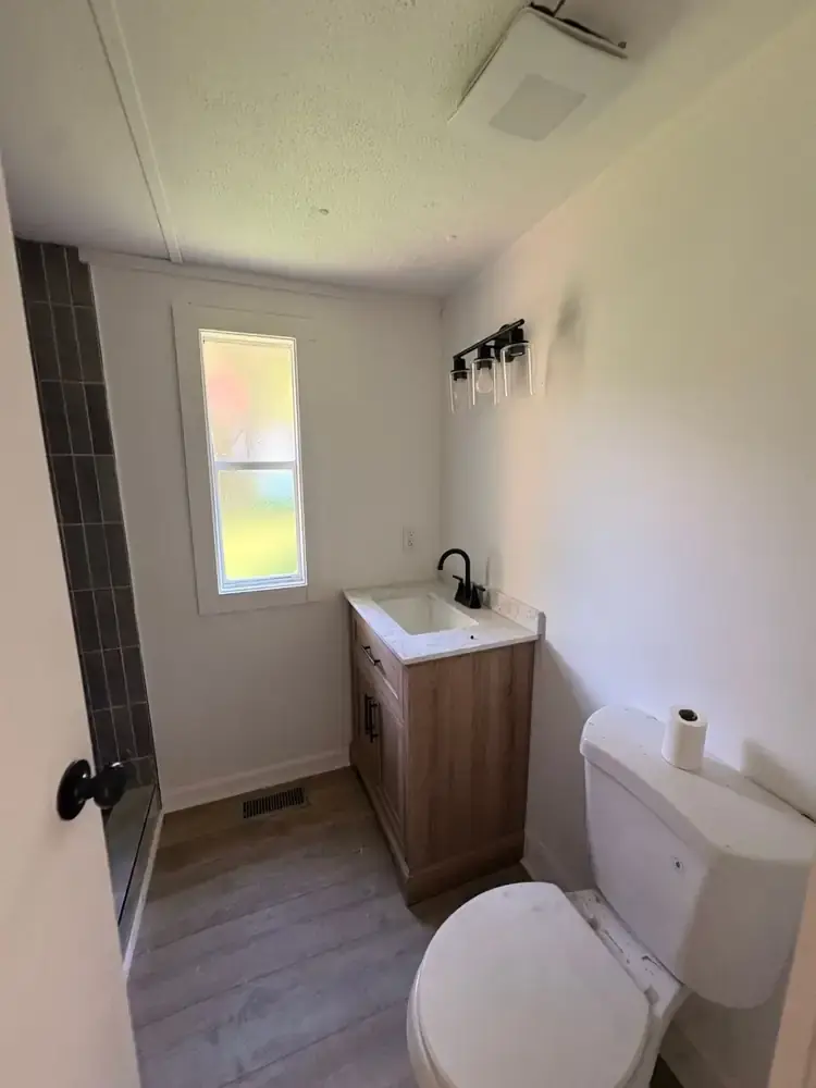 Bathroom with a vanity, toilet, window, and tiled shower surround at 495 Pack Road in Ranger